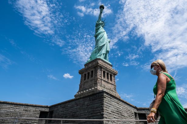 A visitor wearing a protective mask walks past the Statue of Liberty