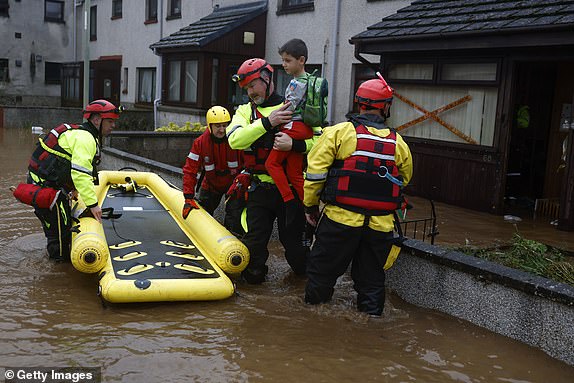 BRECHIN,SCOTLAND - OCTOBER 20: A member of the coastguard carries a young boy out of a house as they help his family to safety from the flood waters on October 20, 2023 in Brechin Scotland. Areas close to the river have been overwhelmed by water which breached the flood defences in the early hours of this morning. Rare Red weather warnings are in place in Scotland and amber warnings in the north of England until Saturday as Storm Babet sweeps the country. (Photo by Jeff J Mitchell/Getty Images)
