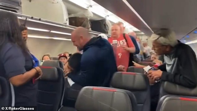 A unruly American Airlines passenger was put in a chokehold by another passenger before being escorted off a plane. (pictured: the disruptive flyer in a chokehold)