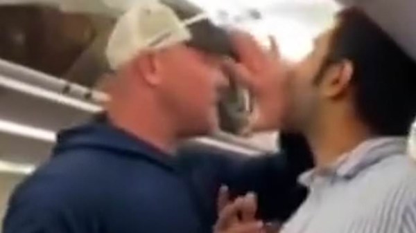 The unruly passenger confronts a man in a baseball cap.
